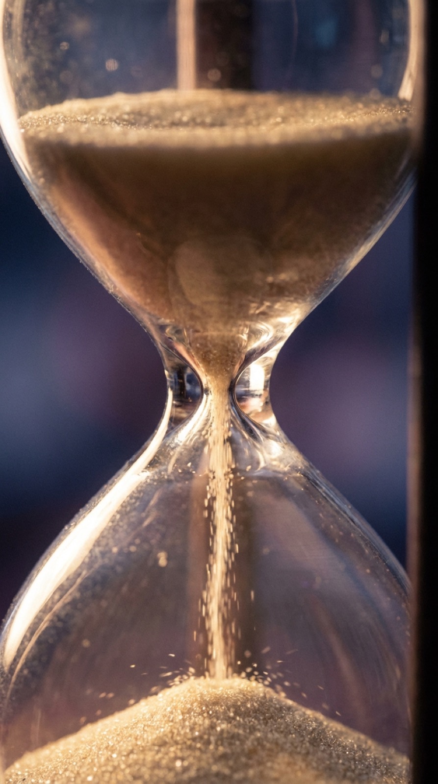 Glass hourglass with drifting amber sand against a dark backdrop